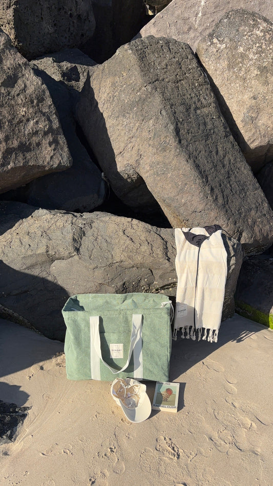 Towelling beach bag packed with beach-day essentials beside coastal rocks