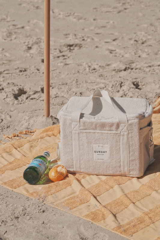 Dunes towelling cooler bag beside a bottle and fruit on a towel at the beach