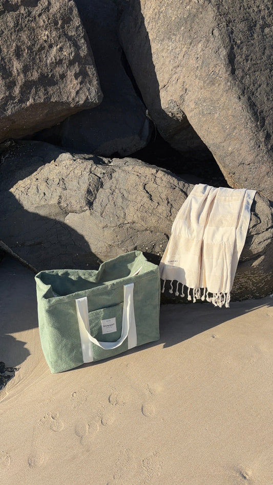 Dunes mesh beach bag beside a towel on sunlit sand