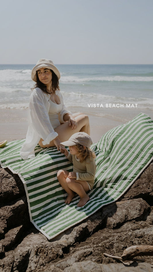 A family relaxing on a green striped Vista Beach Mat beside the coast.