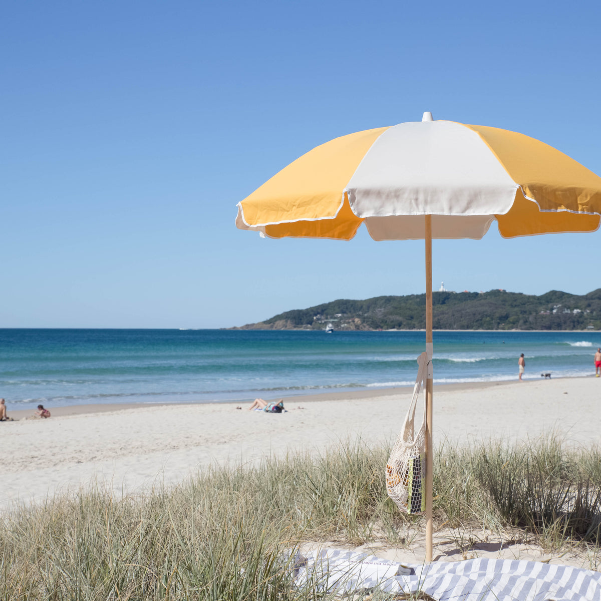 Golden Splice Beach Umbrella with yellow and off-white panels beside dune grass