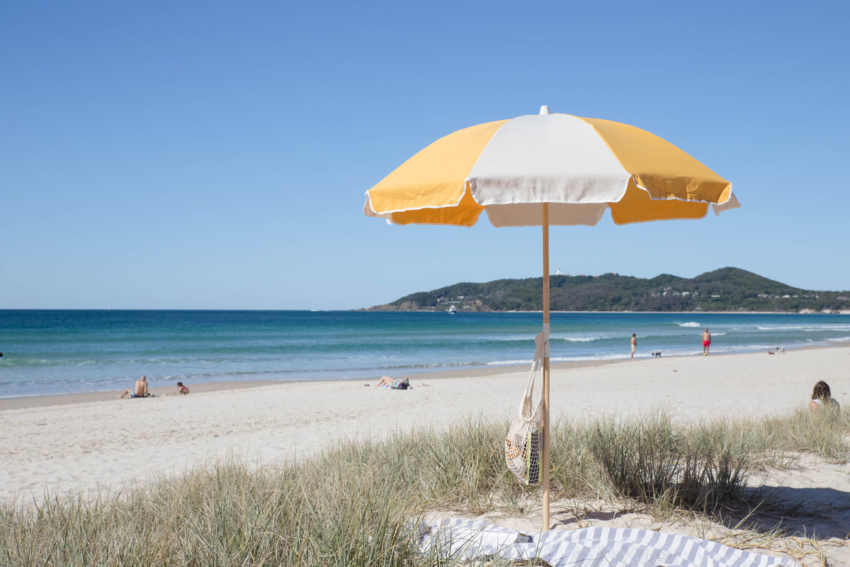 Golden Splice Beach Umbrella with yellow and off-white panels beside dune grass