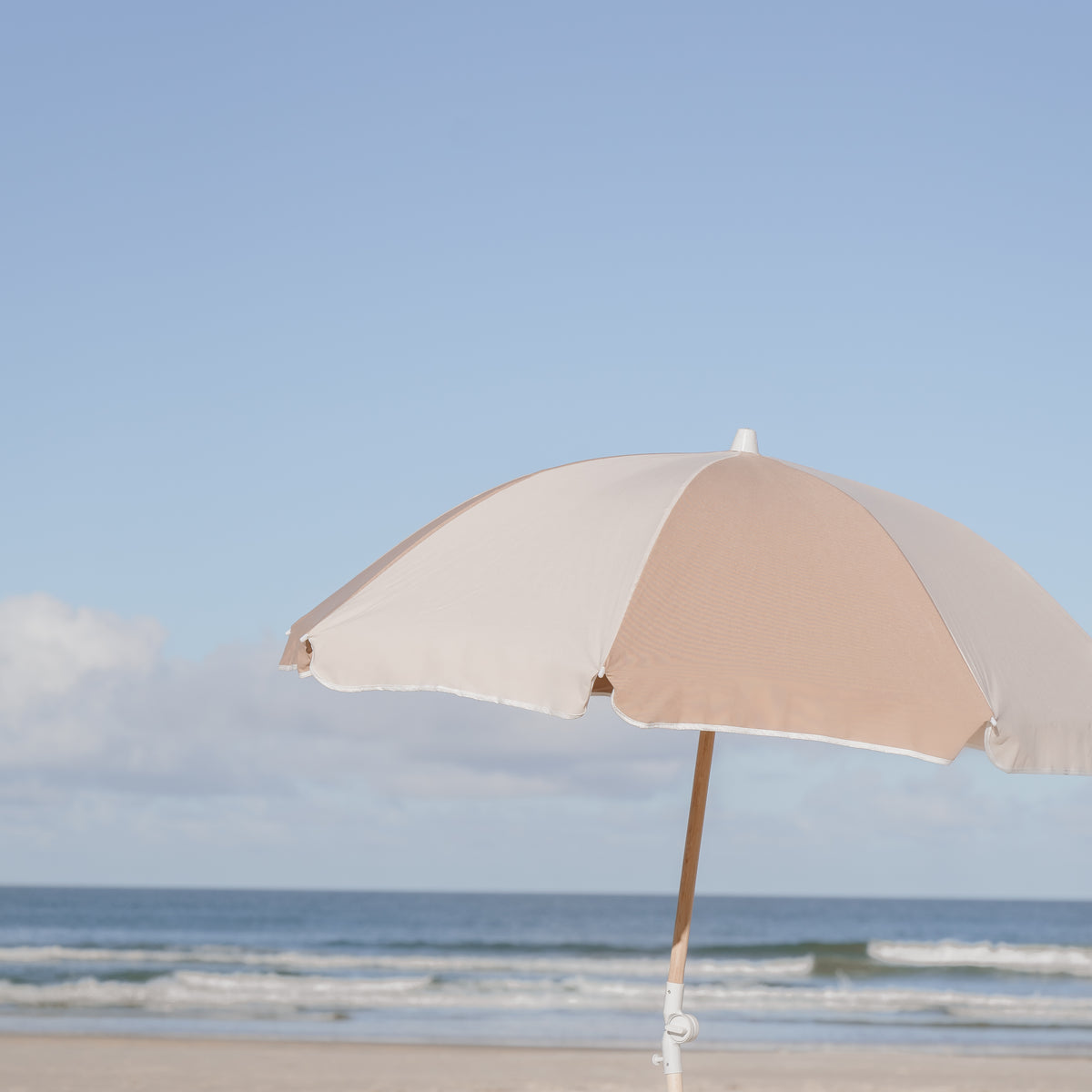 Husk Splice Beach Umbrella with tan and off-white panels beside the ocean