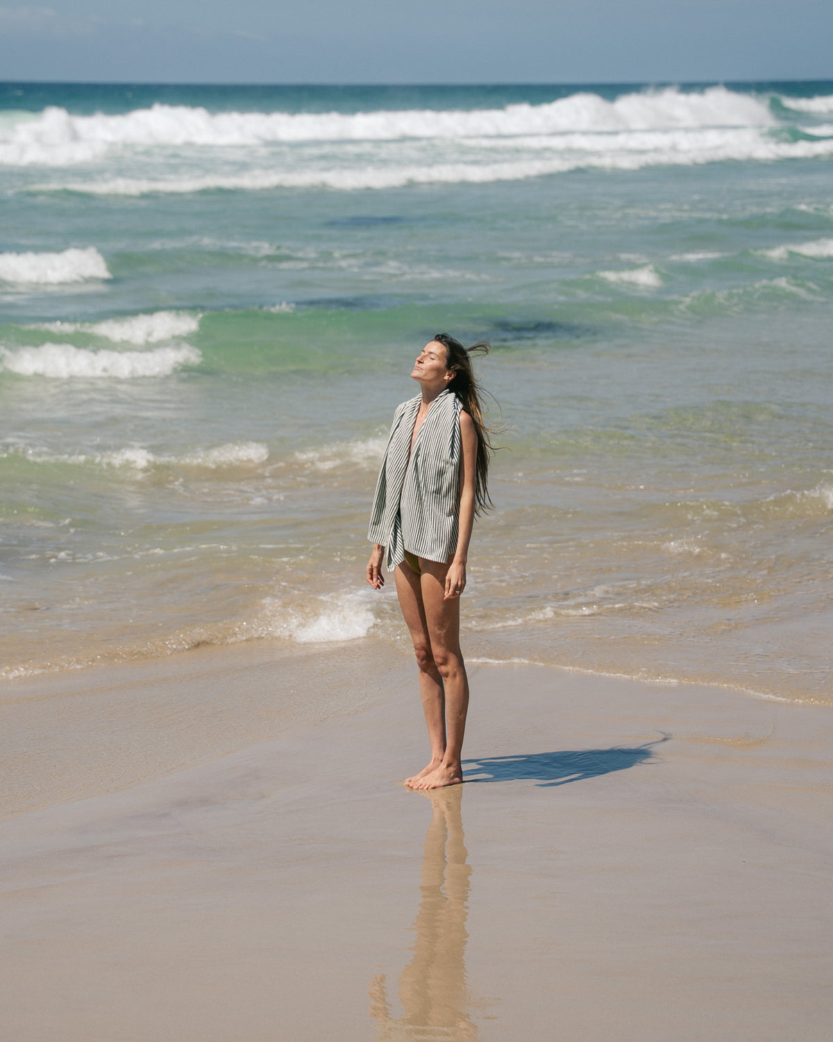 Native striped beach towel draped over a model's shoulders at the shoreline.